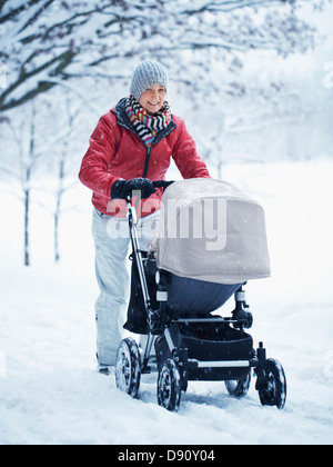 Smiling mother walking with pram at winter landscape Stock Photo