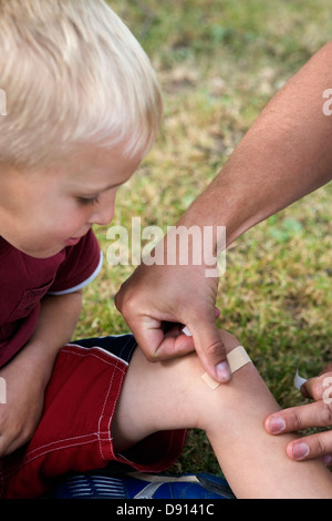 A father putting on a plaster on the knee of his son, Sweden. Stock Photo