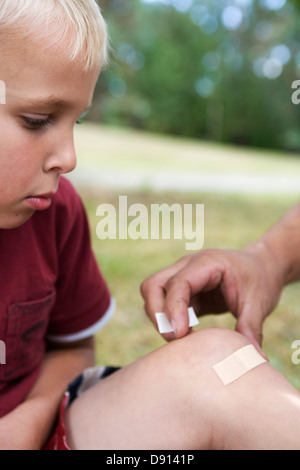 A father putting on a plaster on the knee of his son, Sweden. Stock Photo