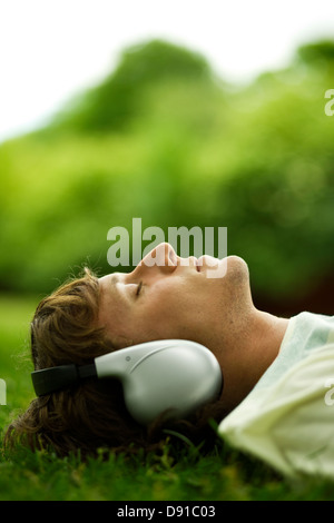 Young man lying in the grass listening to music, Sweden. Stock Photo
