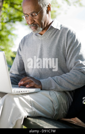 Senior man using a laptop in a park, Sweden. Stock Photo