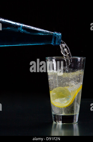 Mineral water is poured into a glass with ice and lemon Stock Photo