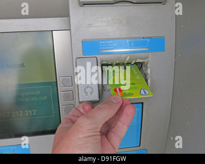 Putting a green Lloyds Avios account card into a co-op cash machine Stock Photo