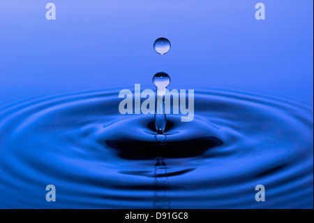 single water drop falling down on blue surface Stock Photo