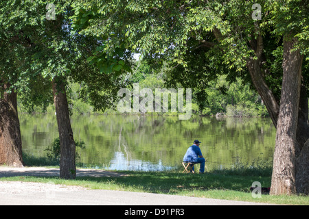 a Caucasian senior man sits on a stool and fishes at Lake Hefner in Oklahoma City, Oklahoma. USA Stock Photo