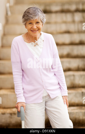 happy elderly lady standing by stairway with cane Stock Photo