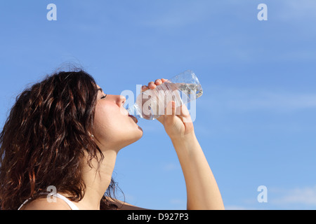 Profile of a woman drinking water from a plastic bottle with a blue sky in the background Stock Photo