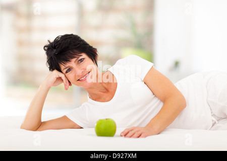 attractive mature woman lying on bed with a green apple in front Stock Photo