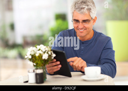 smiling middle aged man surfing the internet using tablet computer at home Stock Photo
