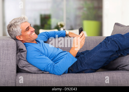 middle aged man reading text message on mobile phone while lying on couch Stock Photo