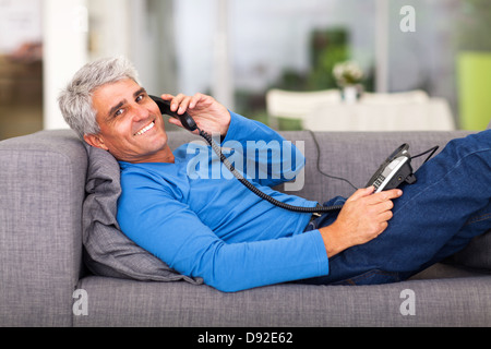 cheerful middle aged man talking on the telephone while lying on sofa Stock Photo