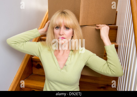 Unhappy woman pauses moving boxes up the stairs in a house Stock Photo