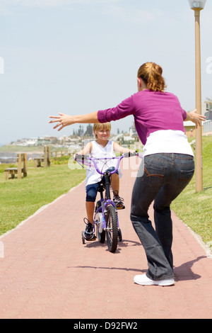 happy little girl riding a bike toward her mother Stock Photo