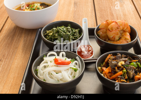 Asian dish on a square plate in black bowls with shrimp, rice noodles, kale (green cabbage) and fried vegetables. Stock Photo