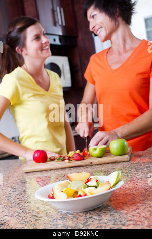 happy middle aged mother and teen daughter cooking in kitchen, focus on fruit salad in foreground Stock Photo