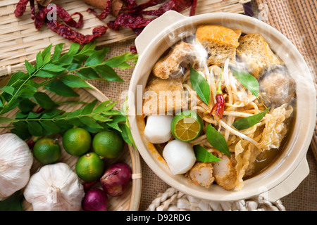 Hot and spicy Singaporean Curry Noodle or laksa mee with hot steam in clay pot, decoration setup, serve with chopsticks. Singapore cuisine. Stock Photo