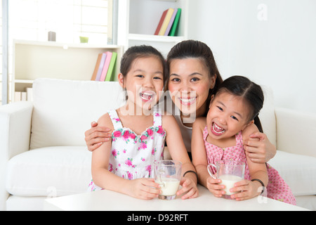 Happy Asian mother and daughters drinking milk at home. Parent and children. Beautiful family model. Stock Photo