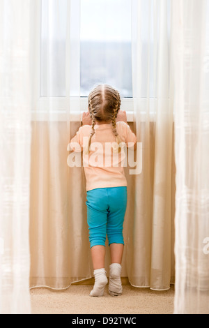 Little girl on her tiptoes trying to see out window Stock Photo