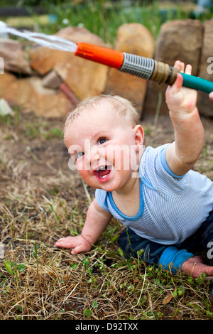 A laughing baby boy holding a garden hose Stock Photo