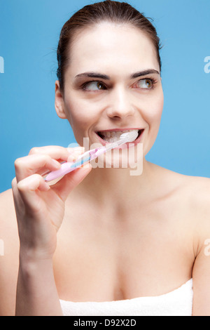 A smiling young woman brushing her teeth while looking away contemplatively Stock Photo