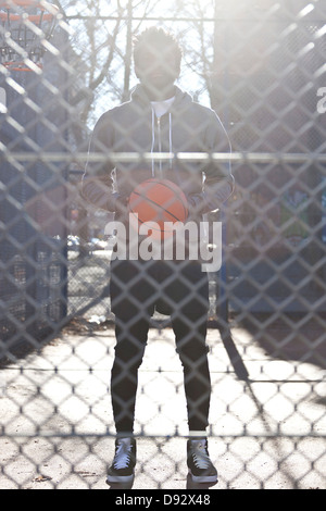 A hip young man holding a basketball and standing on an outdoor basketball court Stock Photo