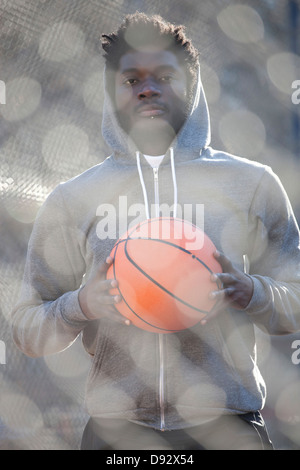 A hip young man holding a basketball and standing on an outdoor basketball court Stock Photo