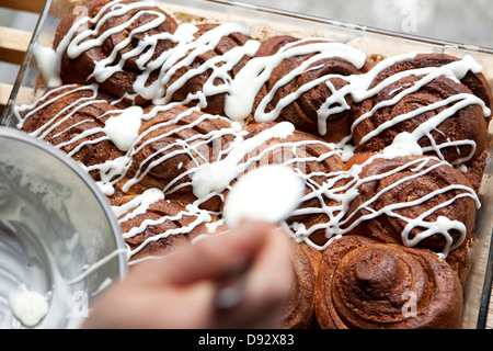 A coffee shop employee putting icing on a cinnamon rolls Stock Photo