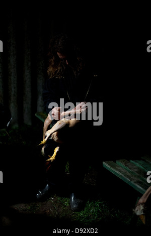 A man cleaning a dead goose in a dark shadowy scene Stock Photo