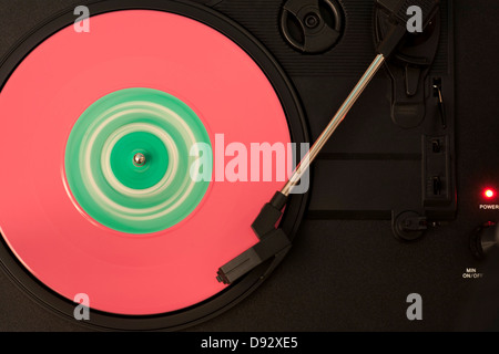 A pink and green vinyl record playing on a turntable Stock Photo