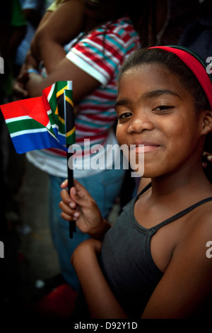 A young African girl smiles waves South African flag as part FIFA world cup final draw festivities on Long Street in Cape Town Stock Photo