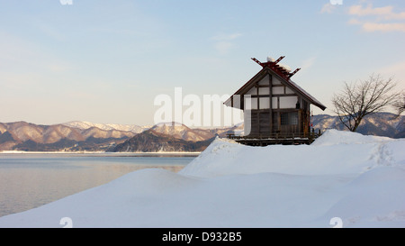 Small Shinto Shrine by the Waters of Lake Tazawa covered in Winter Snow Stock Photo