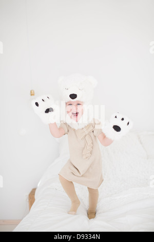 Girl wearing polar bear costume jumping on bed Stock Photo