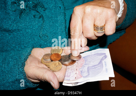 An old / elderly / senior woman’s hands, holding and counting British money, by way of UK pound / pounds sterling notes and coins. Stock Photo