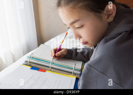 Mixed race girl doing homework on bed Stock Photo