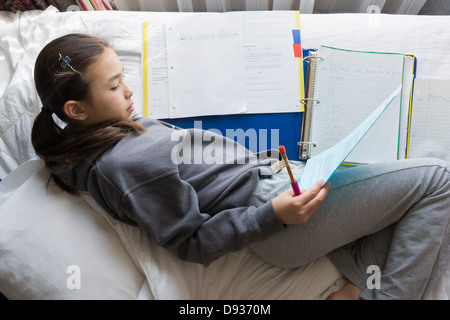 Mixed race girl doing homework on bed Stock Photo