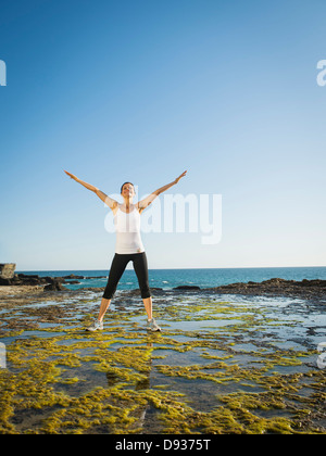 Mixed race runner stretching on rocky beach Stock Photo