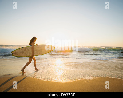 Mixed race woman carrying surfboard on beach Stock Photo