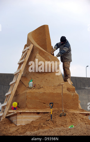 A man building a sand sculpture down at Brighton's Black Rock, part of the Sand Sculpture Exhibition Stock Photo