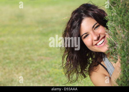 Beautiful woman peeking through a tree and smiling with a green grass background Stock Photo