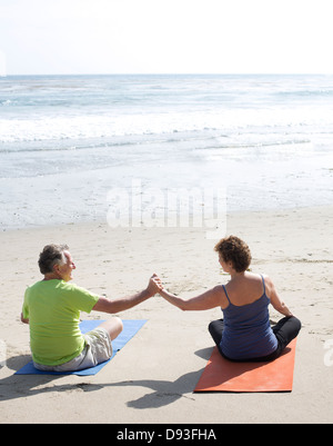 Caucasian couple practicing yoga on beach Stock Photo