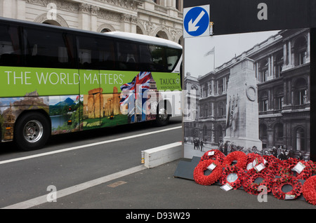 As a tourist bus with an image of Stonehenge on its side passes-by real remembrance wreaths on the ground at the foot of a black and white vintage era photograph that shows the Cenotaph, currently hiding the real monument being renovated in London's Whitehall. Stock Photo