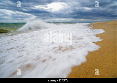 The sea waves splashing over the shore on a sunny day with a blue sky ...