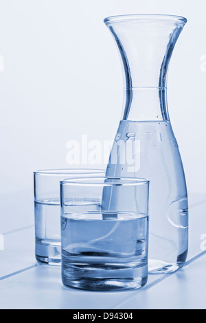 Water Carafe and Two Glasses - a carafe of water on a table with two glasses, blue toned. Stock Photo