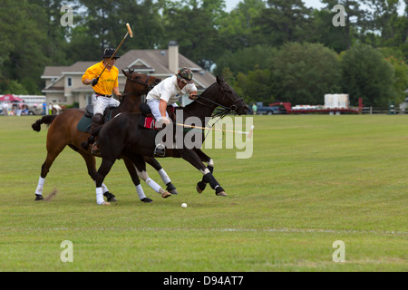 Defending player attempts to strike the ball with his mallet during a polo match. A member of the opposing team follows. Stock Photo