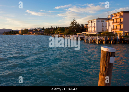Sunset view of the jetty port and Sirmione waterfront on Lago di Garda, Italy. Warm light over the landscape at lake Garda. Stock Photo