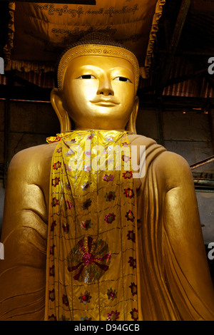 A gold seated Buddha with an embroidered silk robe, covered in dust in one of the small temples on the stairway up Mandalay Hill Stock Photo