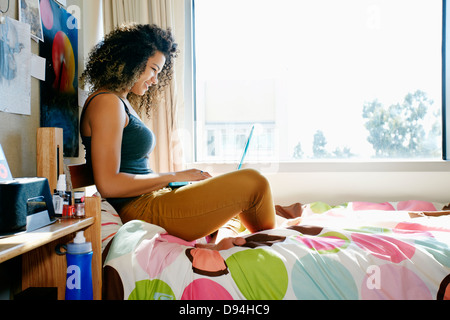 Mixed race college student using laptop in dorm Stock Photo