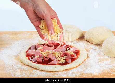 Cook sprinkling shredded cheese over pizza Stock Photo