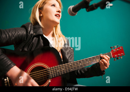 Woman Playing Acoustic Guitar and Singing in Studio Stock Photo