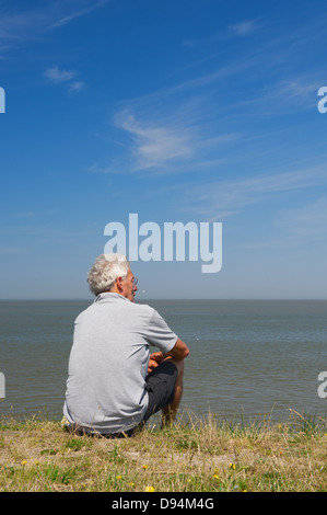 Elderly man is sitting on Dutch dyke in Lauwersoog Stock Photo